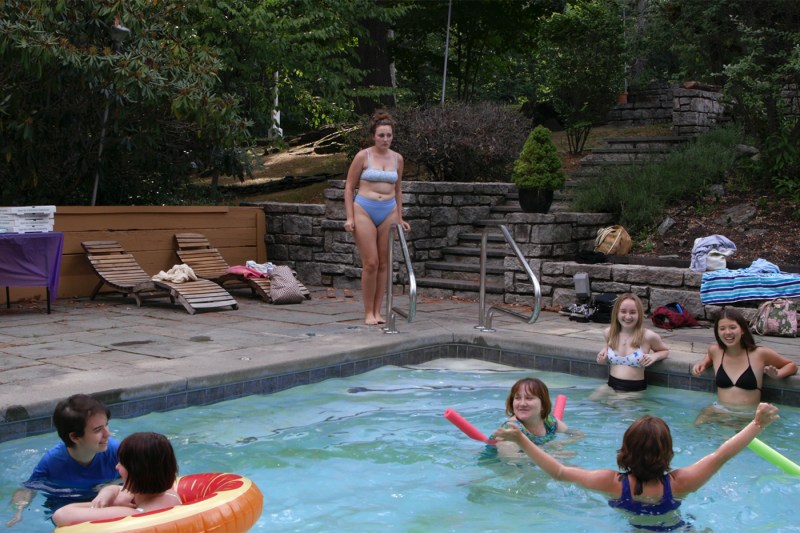 Catherine Argyrople standing shyly next to a pool as multiple children play inside it. 