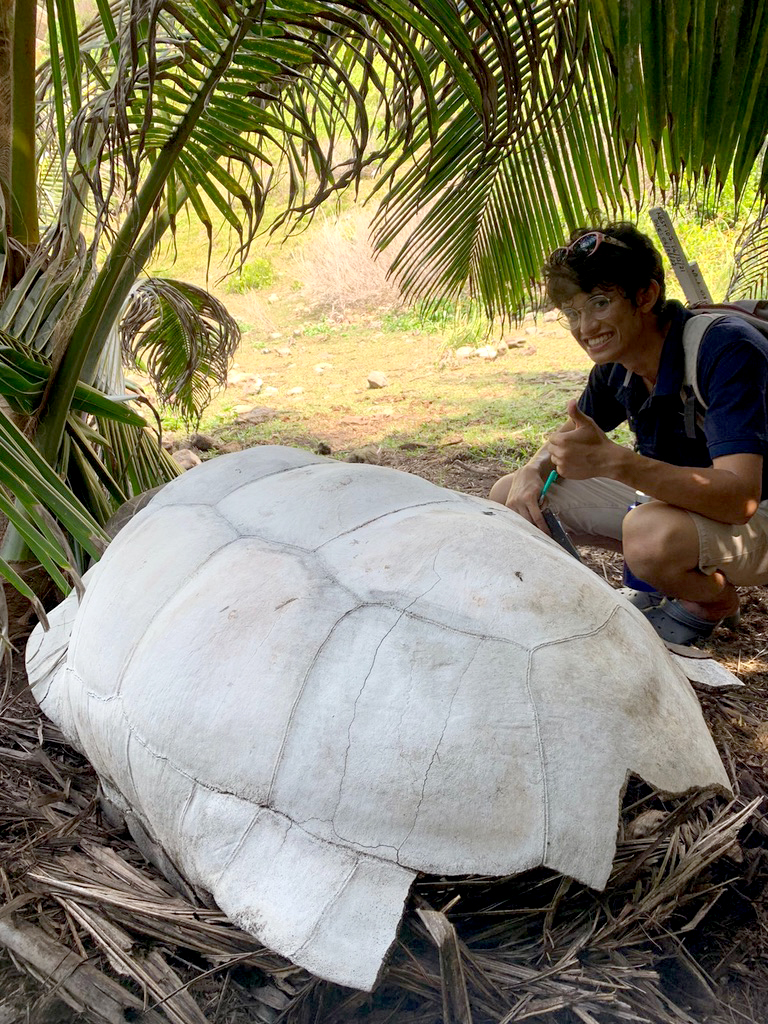 Van Der Sande squatted next to a large tortoise shell giving a thumbs up.