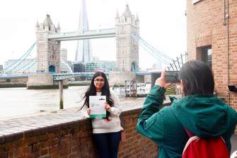 A student poses with their essay in front of the Tower Bridge in London.