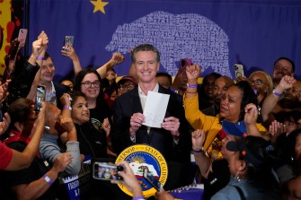 Gavin Newsom holding up a piece of paper and smiling.