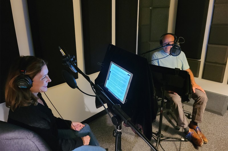 Paula Caligiuri and Andy Palmer in a recording studio sitting in front of microphones with headphones on.