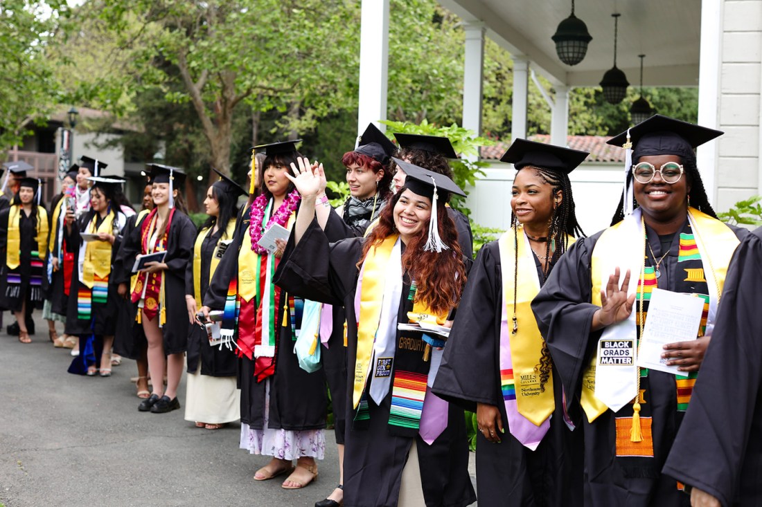 Graduates in regalia stand in a line outside at Northeastern's Oakland commencement. 