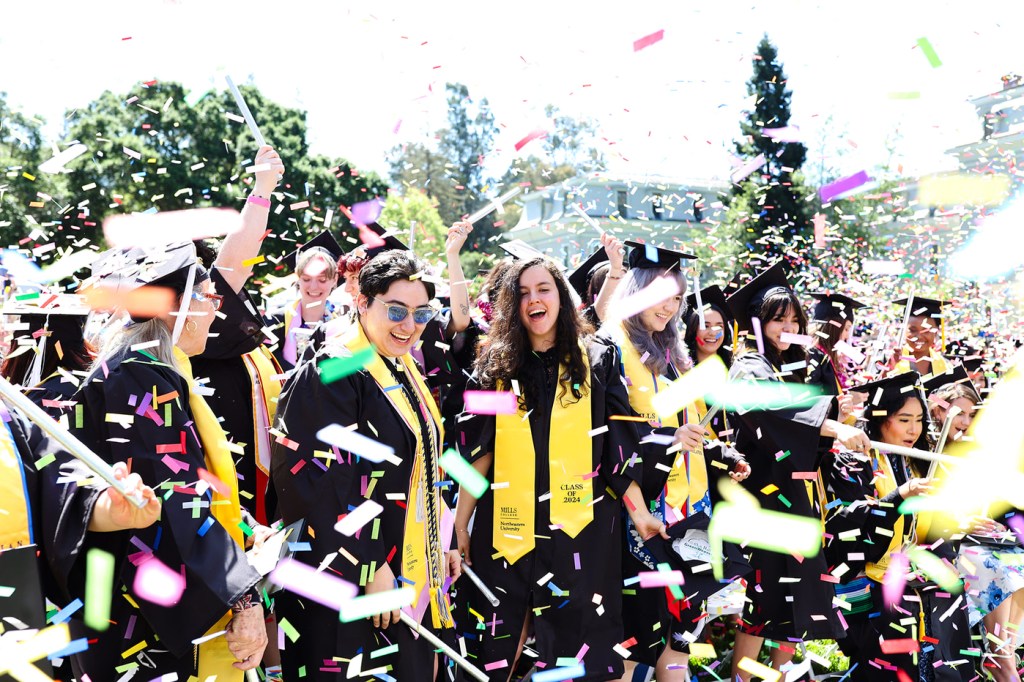 Graduates celebrate at Northeastern’s Oakland commencement while confetti falls around them.