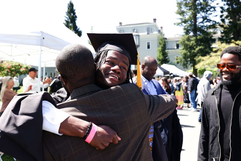 A graduate in regalia receives a hug from another person.