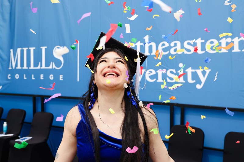 A person wearing a graduation cap smiles while confetti falls on them. 