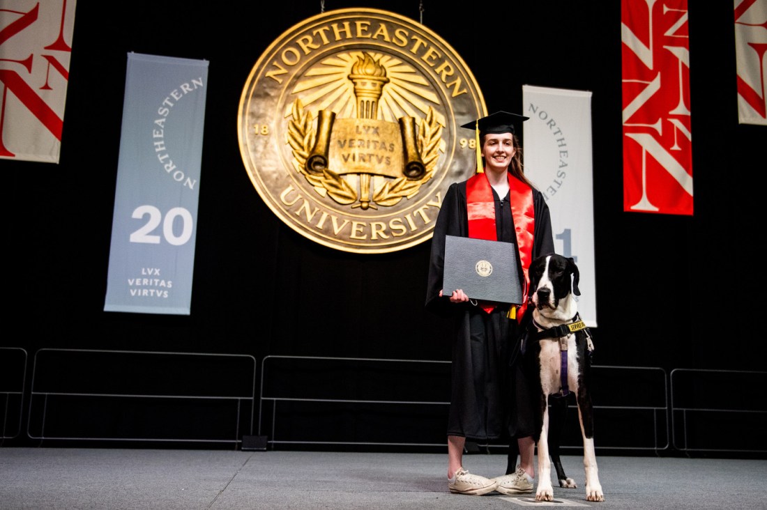 Fiona Howard, wearing regalia, poses with her service dog during Northeastern's commencement ceremony.