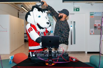 The Northeastern husky mascot Paws putting on headphones behind a DJ booth.