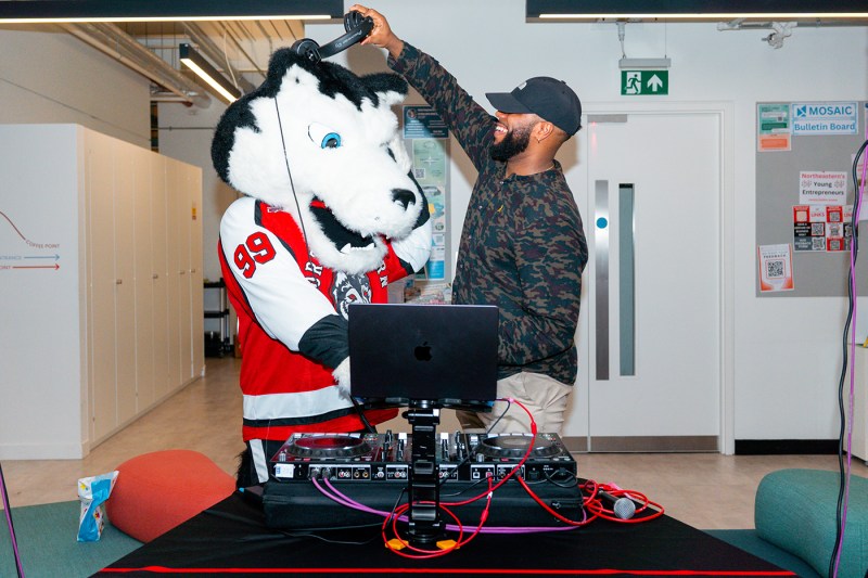 The Northeastern husky mascot Paws putting on headphones behind a DJ booth.