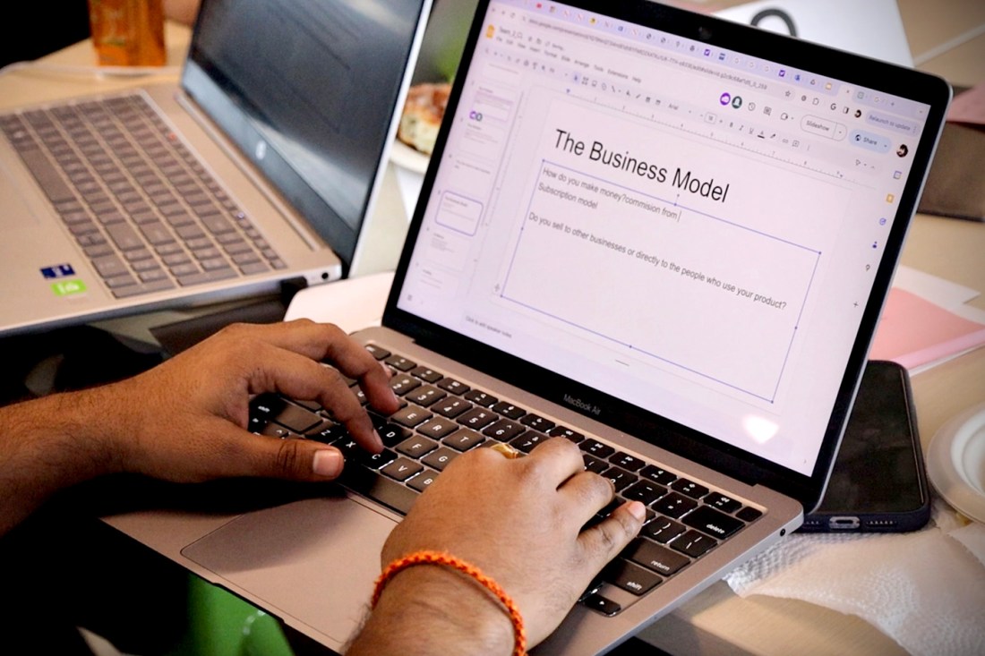 A person typing on their Mac laptop on a PowerPoint slide titled 'The Business Model'.