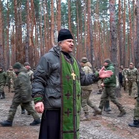 A Russian Orthodox Church priest gesturing while speaking to soldiers outside.