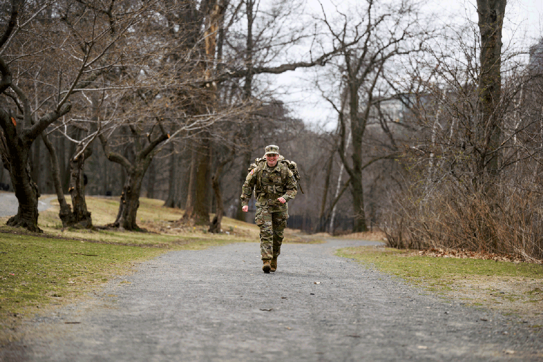 Kayla McCann running on a road, wearing a uniform and military backpack.