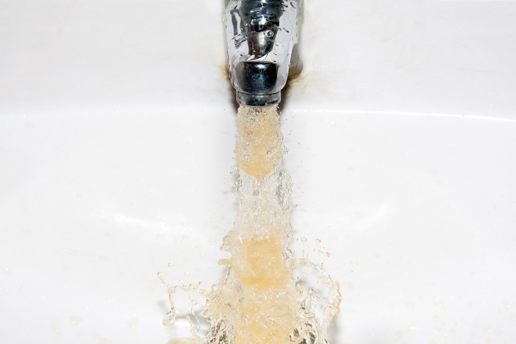 Brown water coming out of a faucet into a white sink.