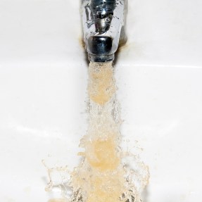 Brown water coming out of a faucet into a white sink.