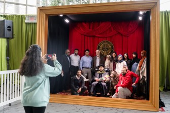Fourteen people pose for a picture inside a life-size picture frame.
