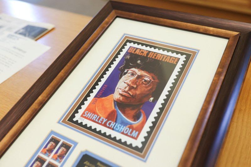 A framed image of a photograph of Shirley Chisholm in the style of a postage stamp saying 'Black Heritage' in all caps at the top and 'Shirley Chisholm' in all caps at the bottom.