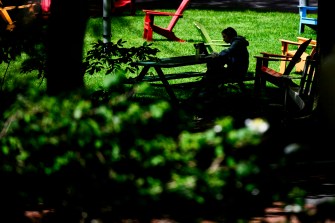 A person sits at a picnic table, which is surrounded by colorful Adirondack chairs, with a laptop.