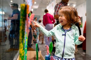 A child wearing a teal-colored sweatshirt points toward art on a wall.