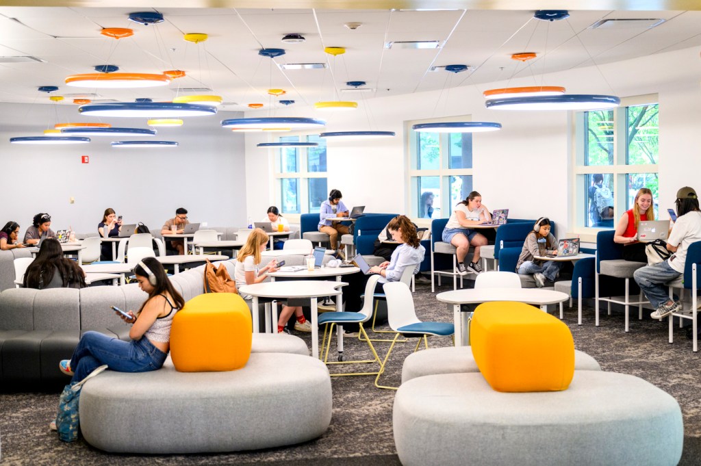 Dozens of people work on their laptops at tables and chairs inside a library.