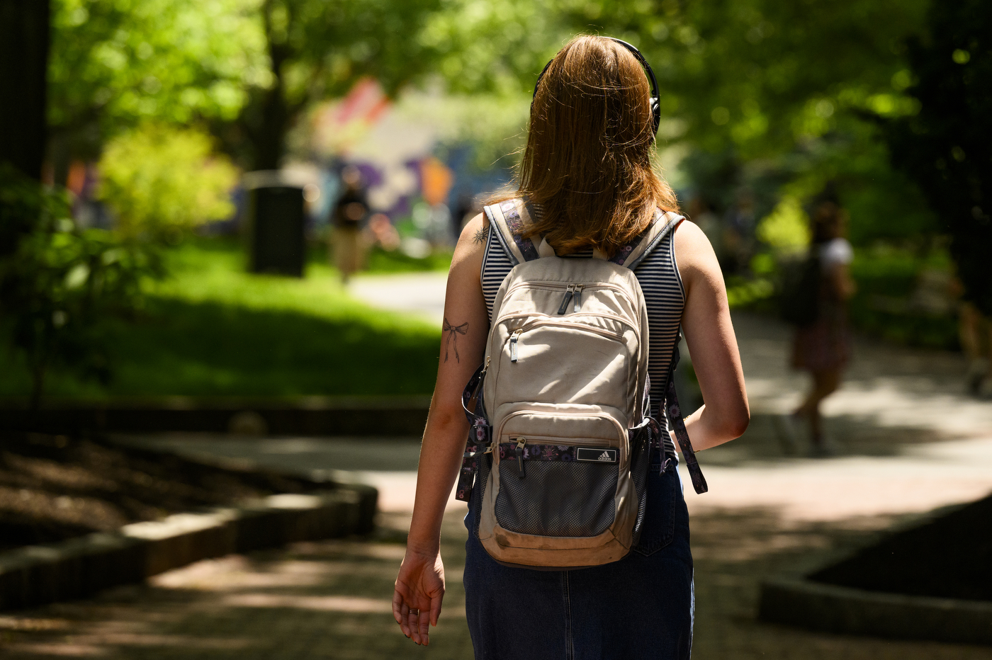 A person with a tan backpack walks around outside on a sunny day. 