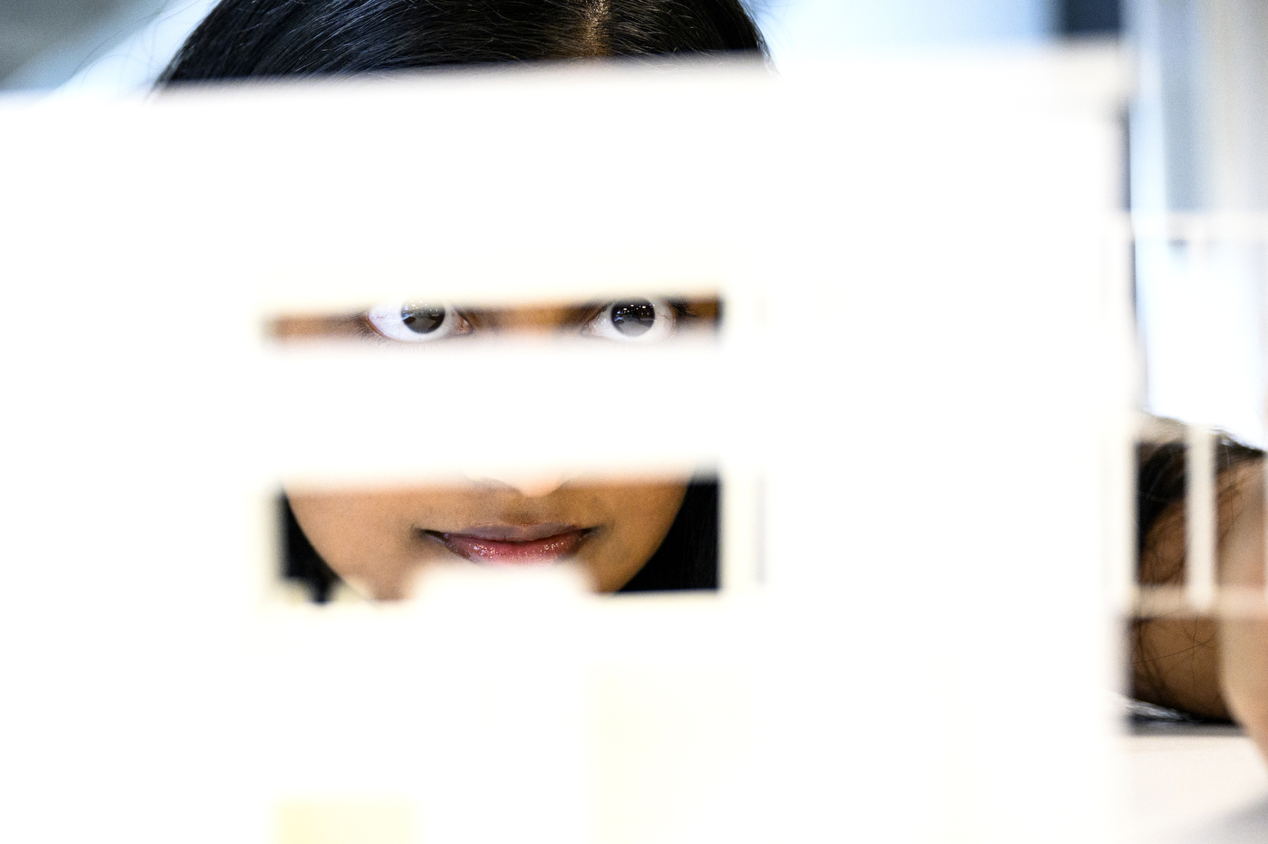 A person looks through slits cut out of a white wall.