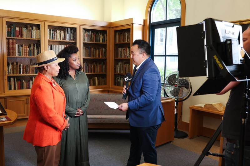 U.S. Rep Barbara Lee and Christina Jackson speaking to a man with a microphone in front of a camera crew.