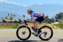 Helena Gilbert-Snyder biking on the road with mountain vistas behind.