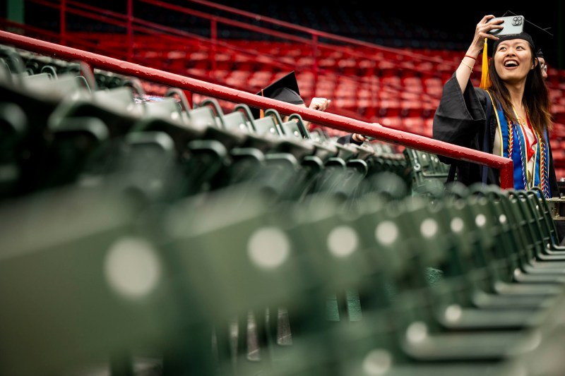 A graduate takes a selfie in the stands of Fenway park