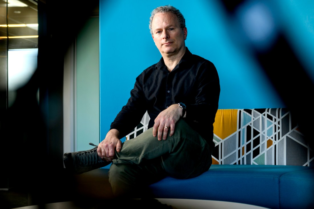 Portrait of David Lazer sitting on a blue couch in front of blue wall. 