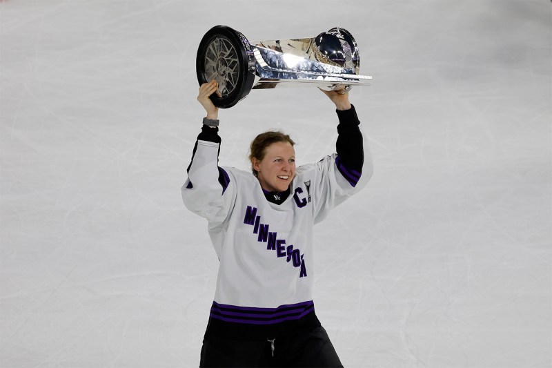 Kendall Coyne Schofield holding a trophy over her head on the rink. 