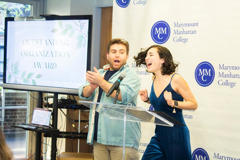 Students clapping and dancing in front of a podium next to a screen that has a presentation slide titled 'Outstanding Organization Award.'