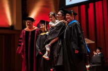 Qingzhao Li and Wen Min holding their daughter Camila in their arms on stage at the Seattle Commencement.