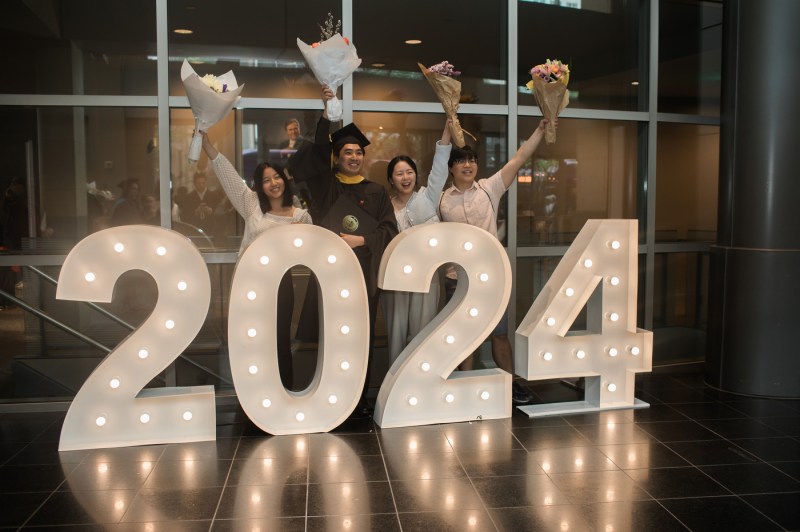 Four people stand in front of a display of large, brightly lit numbers: "2024". 