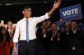 Rishi Sunak wearing a white shirt and blue tie waving at an election campaign.