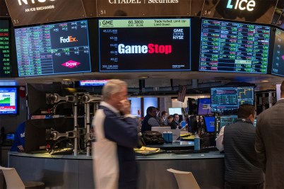 Traders walking on the floor at the New York Stock Exchange in front of a screen displaying the GameStop logo.