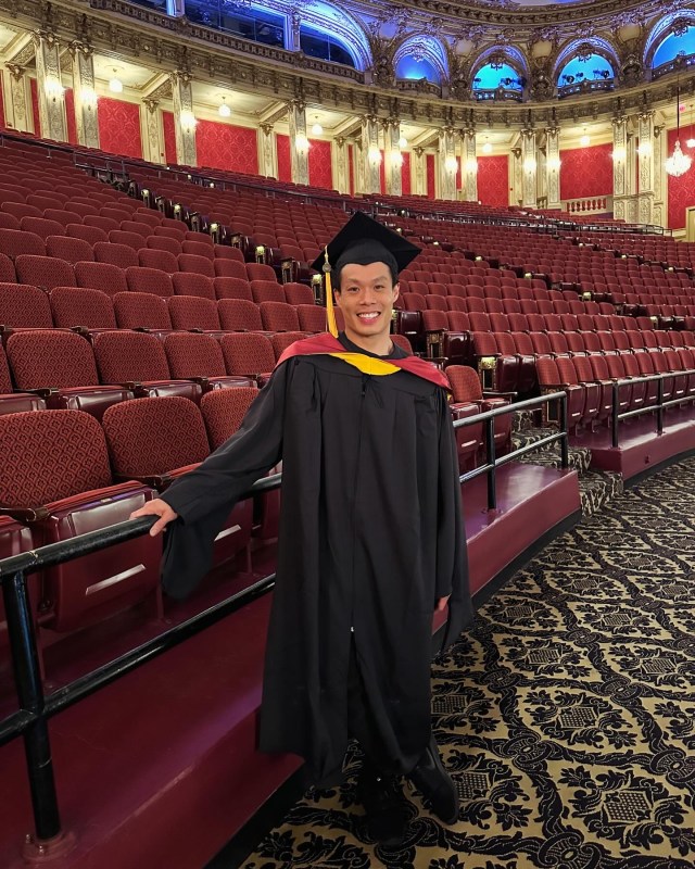 Jon Lam in graduation regalia, smiling in an empty theater.