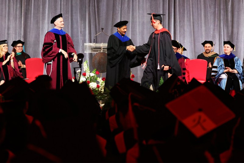 A graduate shaking hands with a faculty member on stage at the 2024 Vancouver convocation.