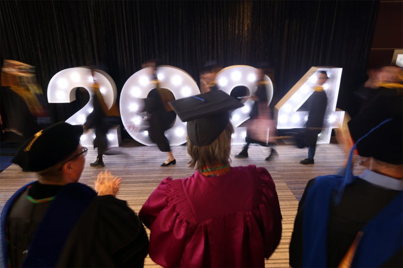 A time lapse photo of graduates walking in front of large 2024 lights.