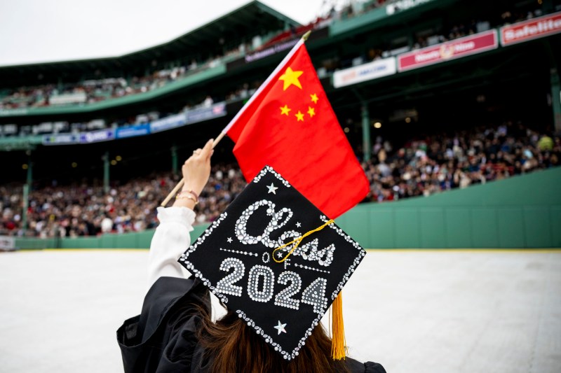 A graduate from behind with Class of 2024 on their mortarboard, holding a Chinese flag