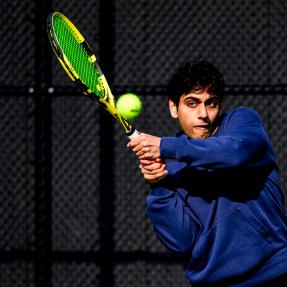 A person wearing a blue sweatshirt hitting a tennis ball with a neon green racquet.