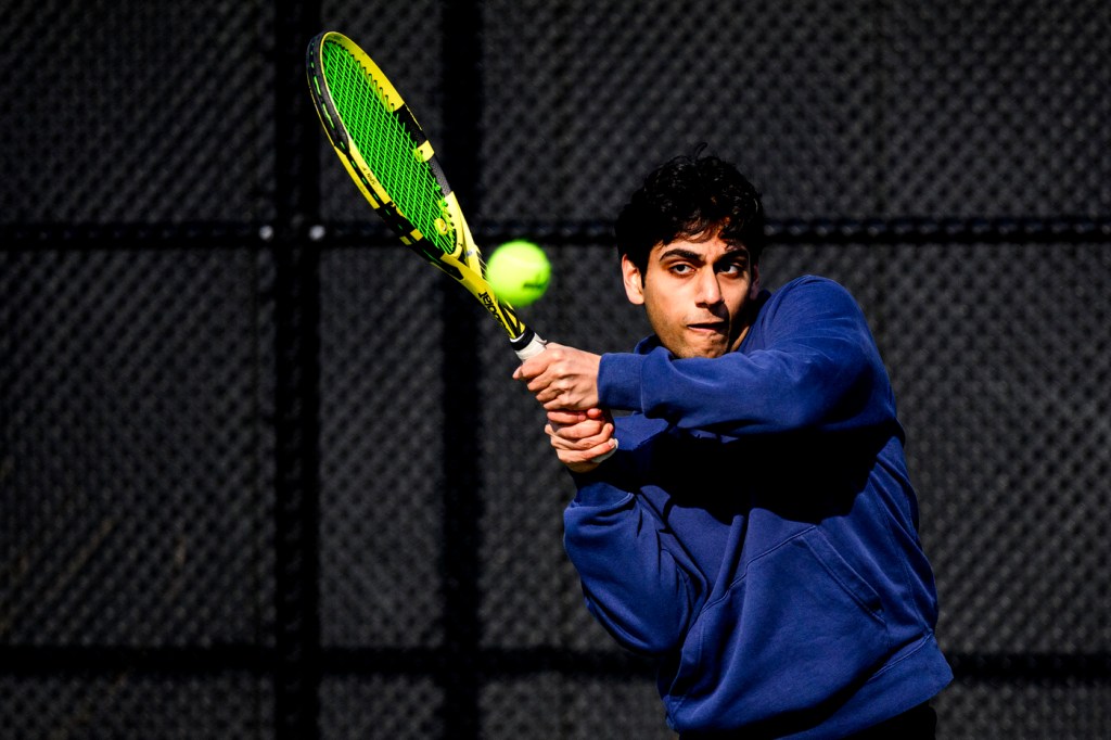 A person wearing a blue hoodie hitting a tennis ball with a neon green racket.