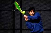 A person wearing a blue sweatshirt hitting a tennis ball with a neon green racquet.