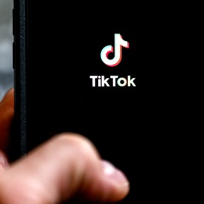 A person holding their phone up to a black screen showing the TikTok logo.