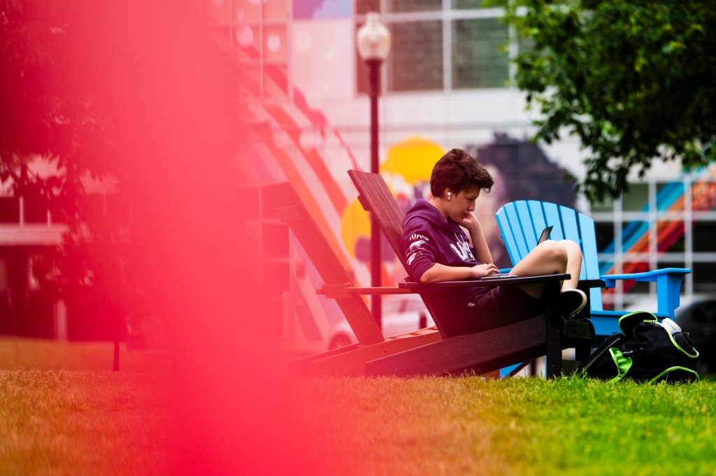 A person sits on an Adirondack chair with a laptop sitting in their lap.