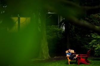 A person reads a book while sitting on a red chair outside on a sunny day.