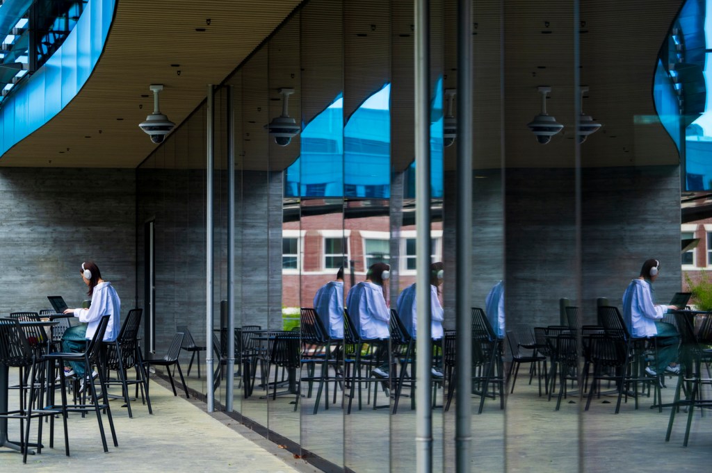 A person wearing headphones works on their laptop while sitting on a patio outside.