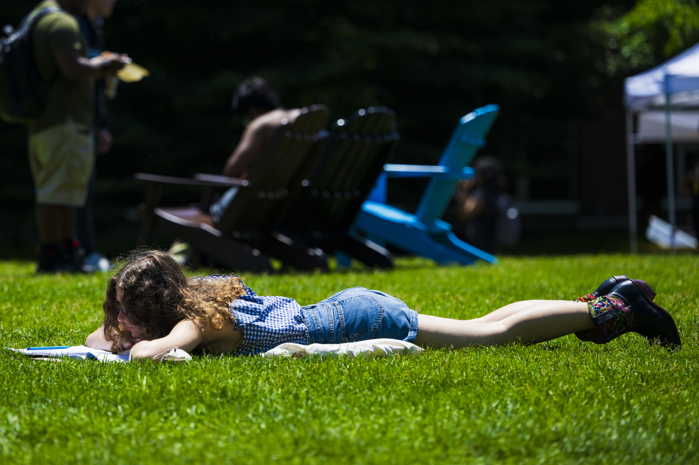 A person reads a book while laying on the ground outside on a sunny day.