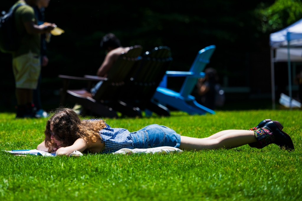 A person reads a book while laying on the ground outside on a sunny day.