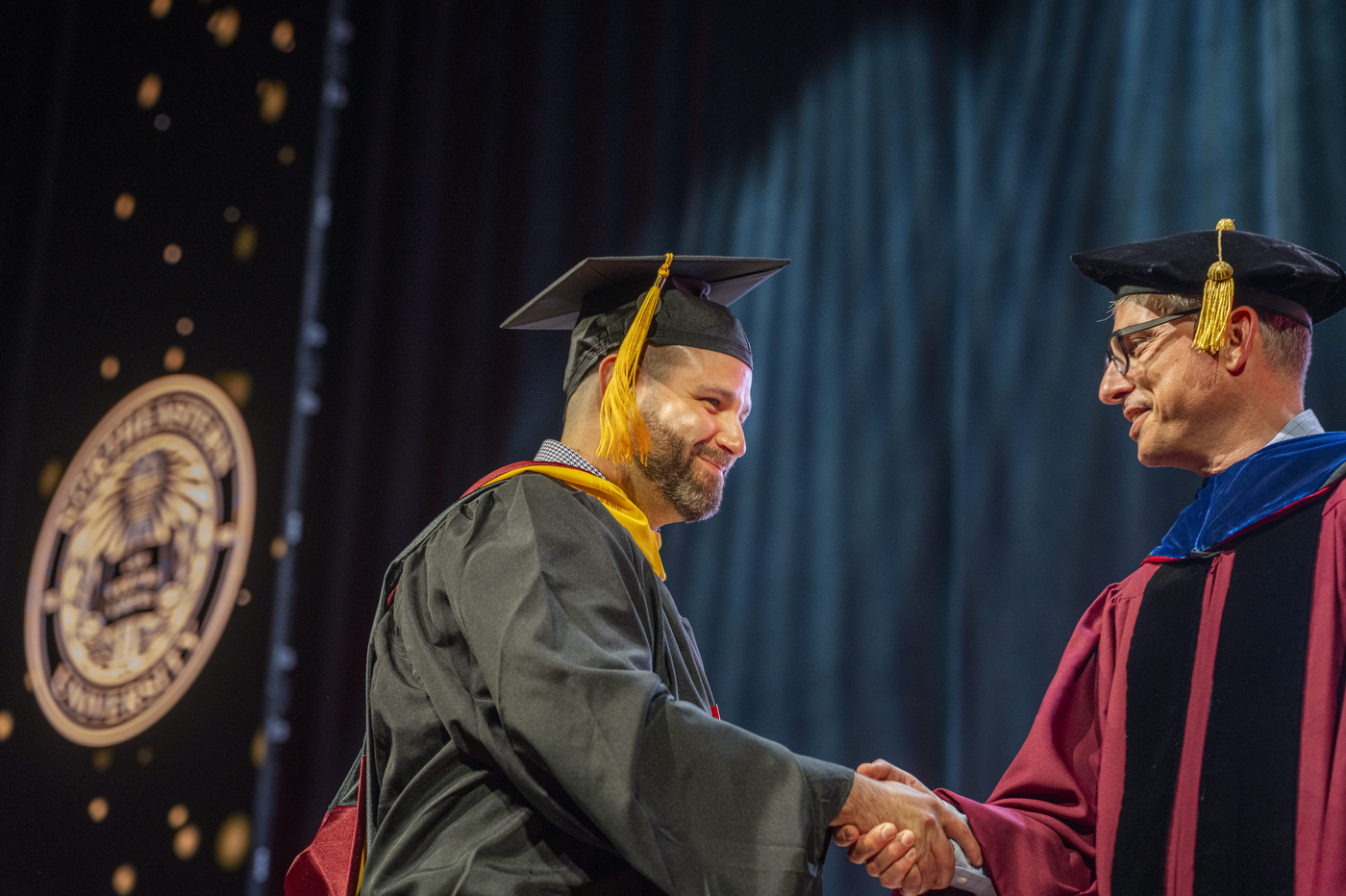 A graduate shaking hands with a faculty member on stage.