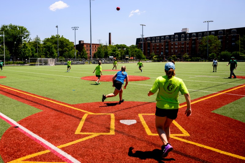 People play kickball on a field outside on a sunny day.
