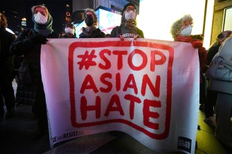 People hold a white sign with red text: "# Stop Asian Hate."